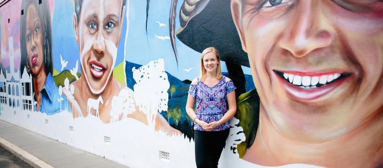 A student against a wall with a colourful mural of faces