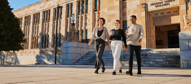 Three people walking outside the Forgan Smith Building at the St Lucia campus.