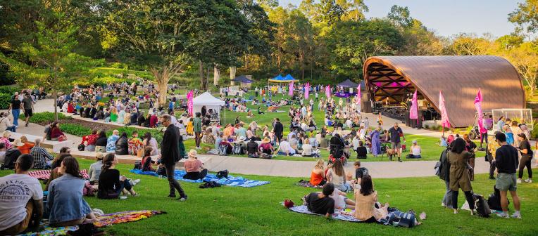 Crowd lounging on the lawns around the UQ Lakes Ampitheatre