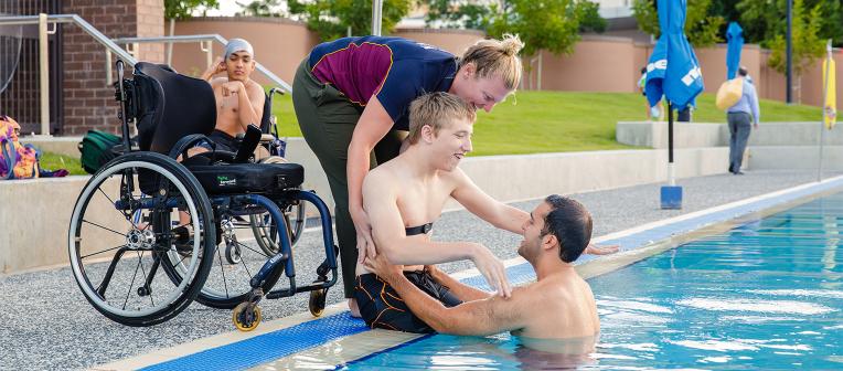 Two UQ staff members help a Para START participant into the pool
