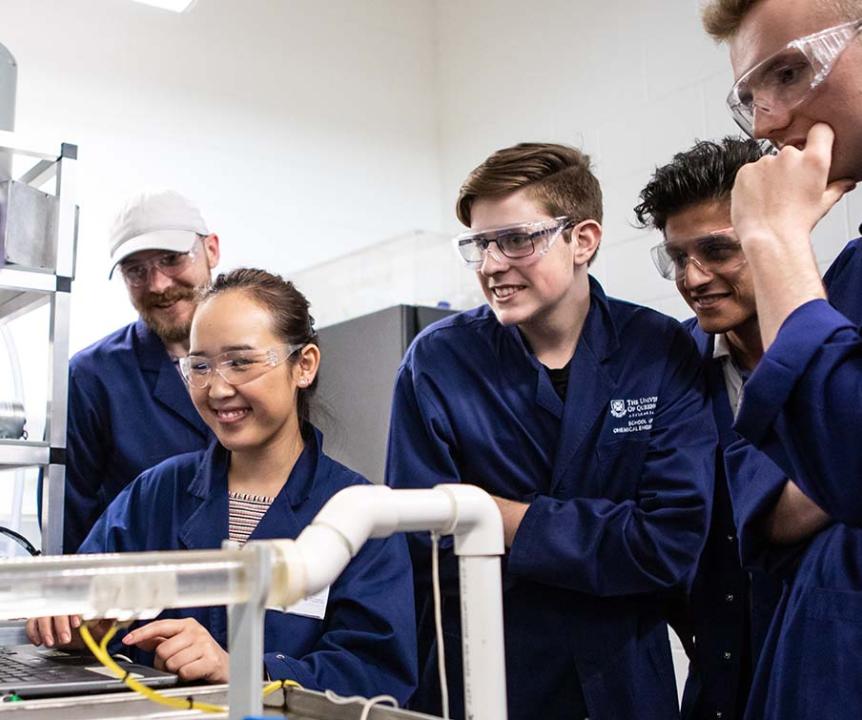 Students in jumpsuits and goggles looking at a computer. 