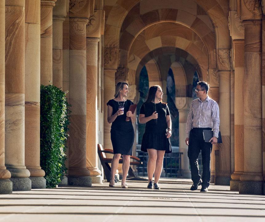 3 staff members walking through the sandstone pillars at UQ