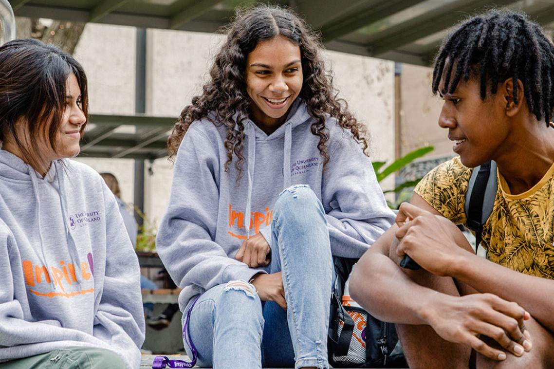 Three students smiling and talking on steps.