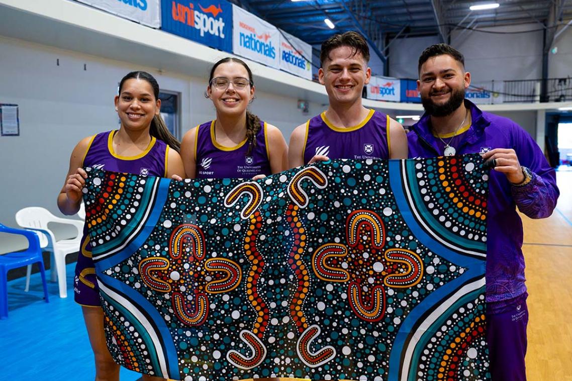 Four UQ competitors in the 2024 Indigenous Nationals holding an Indigenous artwork