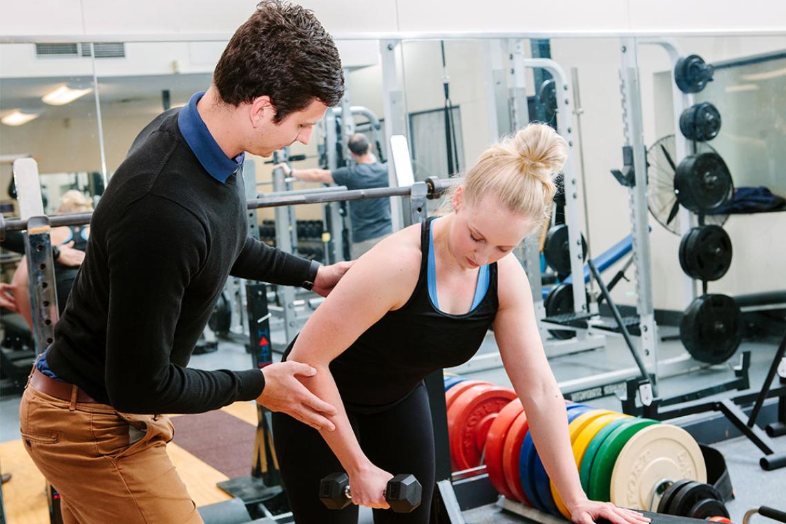 Physio helps women lift a weight in the gym