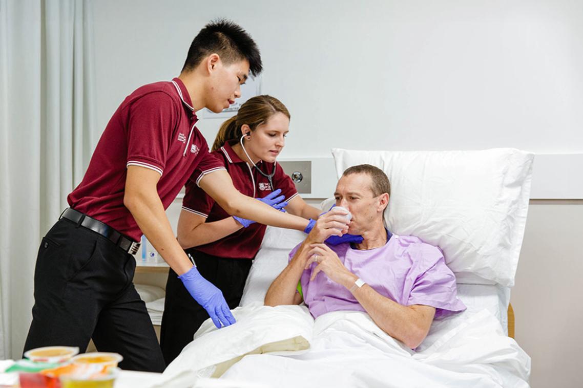 2 practitioners help a patient on a hospital bed