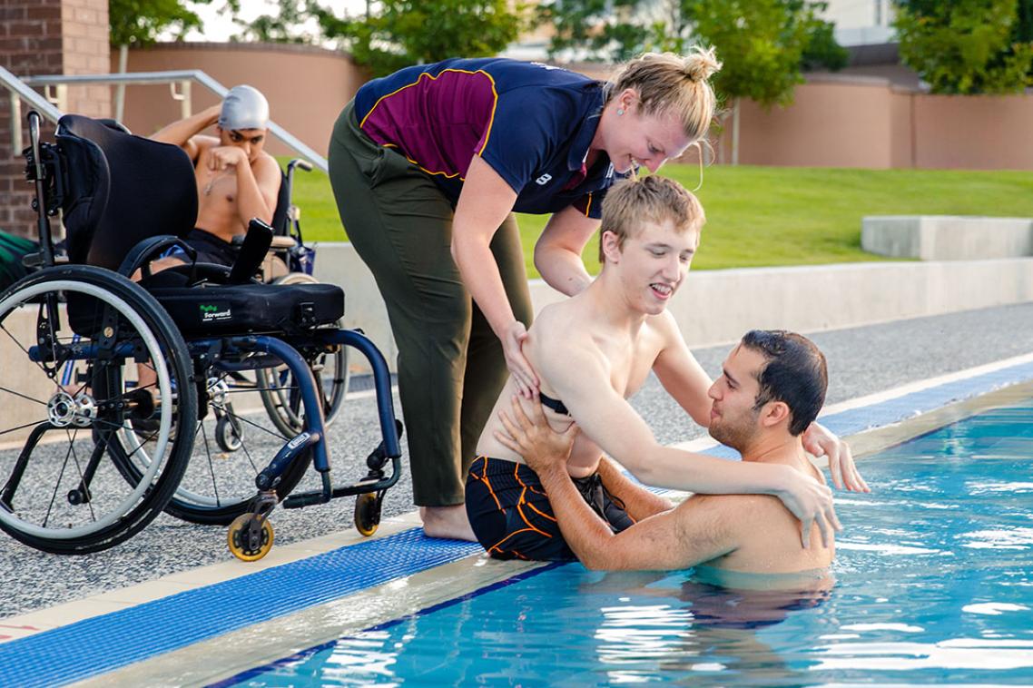 Young man with cerebral palsy being assisted into a pool