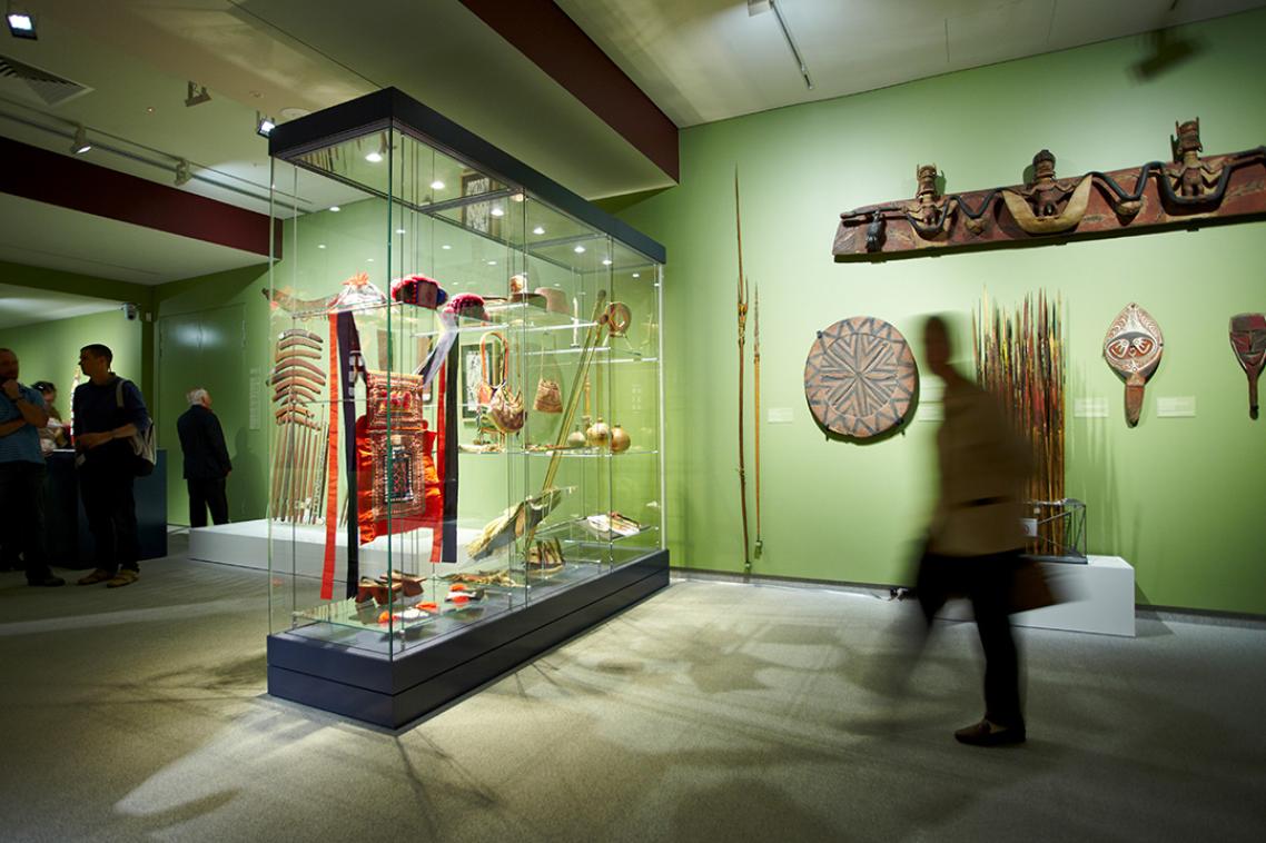 A room, with green walls, houses anthropological artefacts in a glass case.