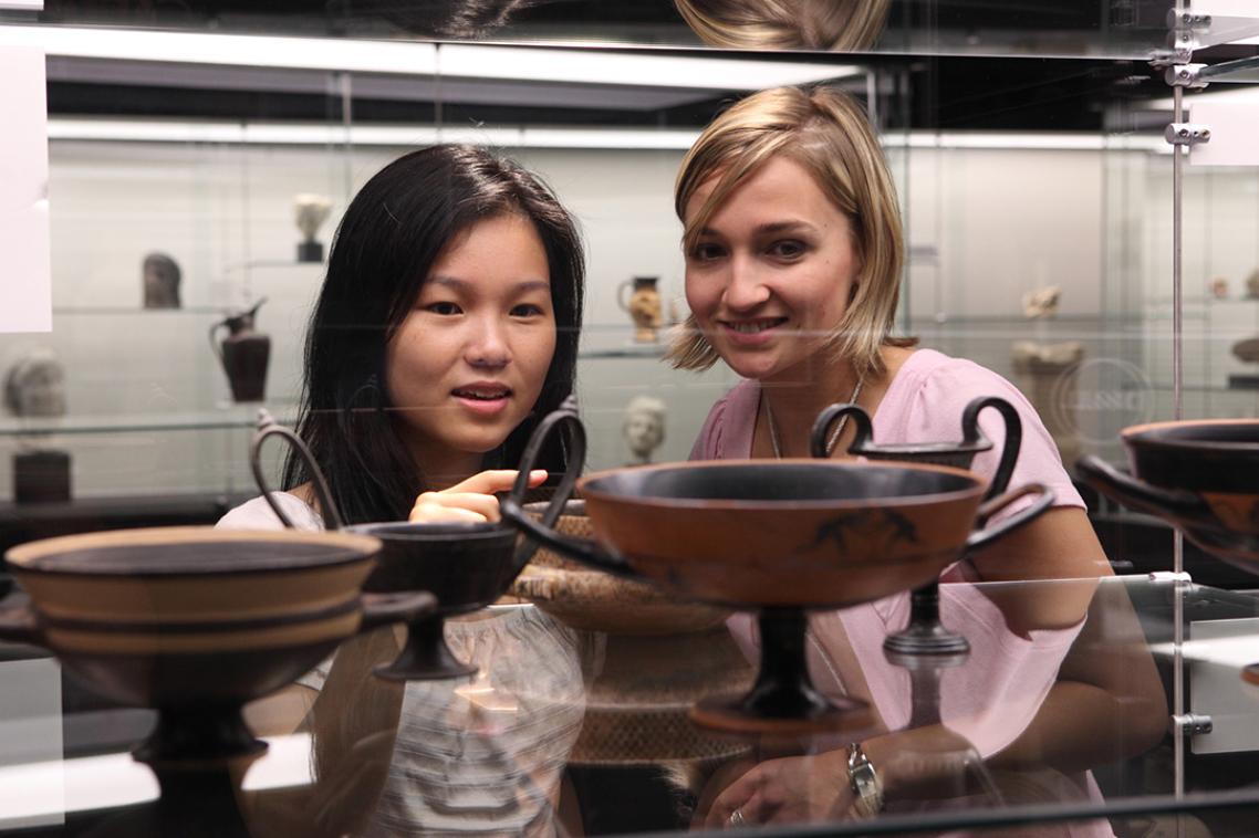 Two people look at a display of clay vessels in a museum setting. 