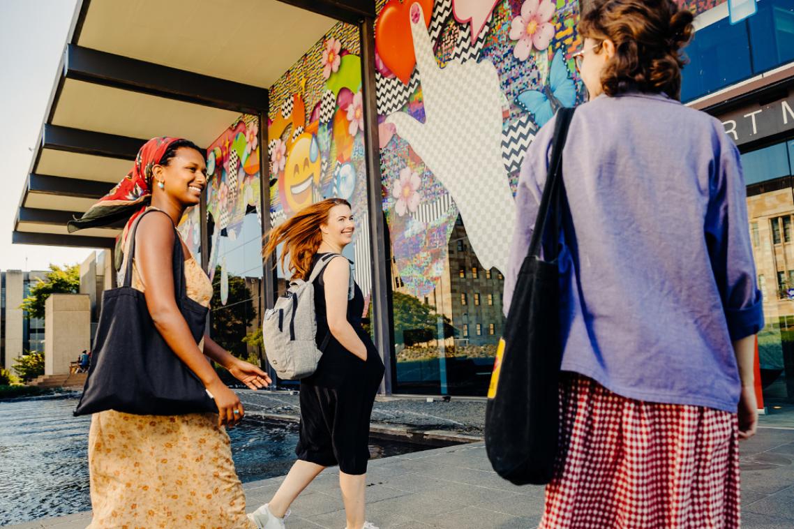 Three women enter a building that has a bright, busy mural on the wall