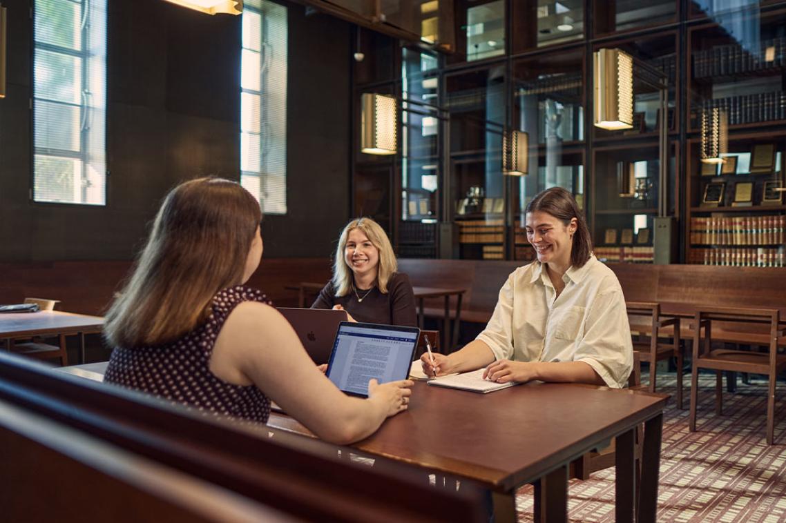 Three students at a study desk in the Law library